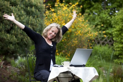 woman working in yard on laptop with arms raised