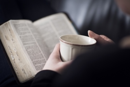 woman holding cup of coffee with Bible open