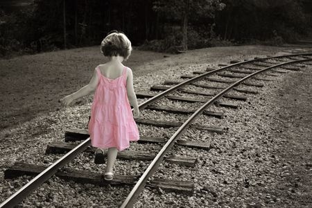 little girl in pink dress walking down train tracks