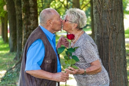 elderly man handing woman a rose while kissing her