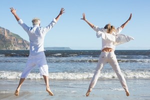 mature couple facing ocean jumping with arms up